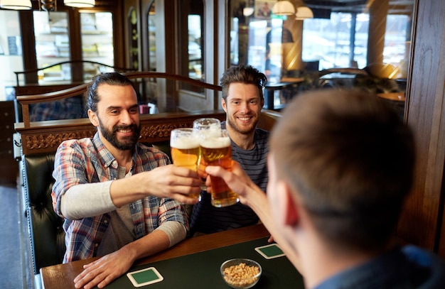 gente, ocio, amistad y concepto de fiesta - amigos varones felices bebiendo cerveza de barril en el bar o pub y vasos tintineantes