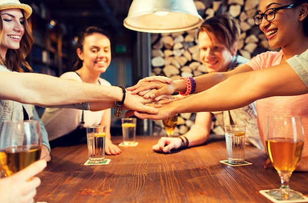 Foto gente, ocio, amistad y concepto de gestos - grupo de amigos sonrientes felices con bebidas poniéndose las manos encima en el bar o pub