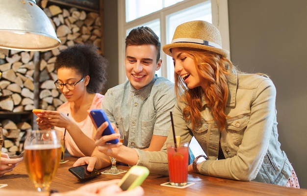 gente, ocio, amistad, tecnología y concepto de comunicación - grupo de amigos sonrientes felices con smartphones y bebidas en el bar o pub