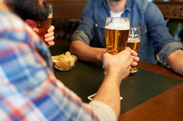 Foto gente, ocio, bebidas y concepto de celebración - amigos varones felices bebiendo cerveza en el bar o pub