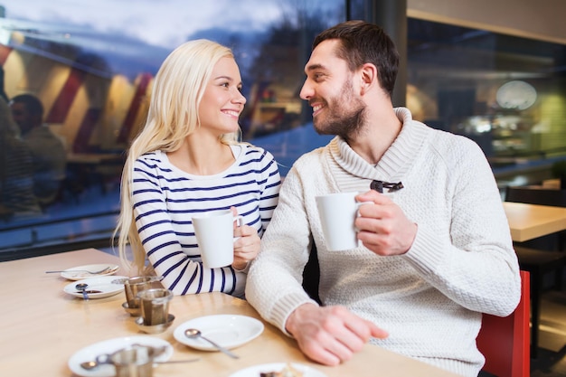 gente, ocio, comunicación, concepto de comer y beber - pareja feliz reuniéndose y bebiendo té o café en la cafetería