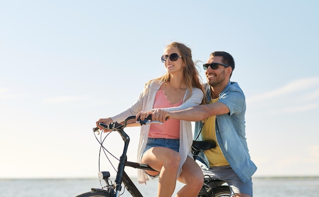 Foto gente, ocio y concepto de estilo de vida - feliz pareja joven montando bicicletas en la playa