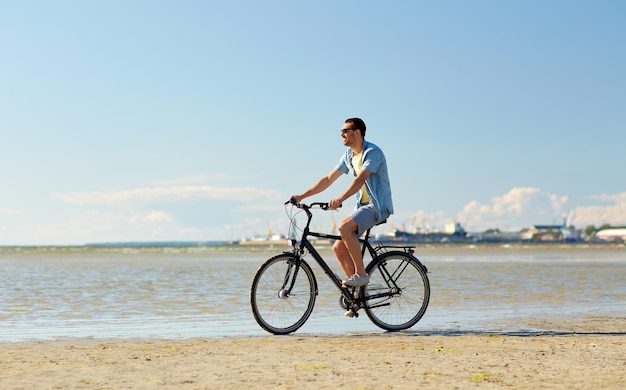 gente, ocio y concepto de estilo de vida - joven feliz montando en bicicleta a lo largo de la playa de verano