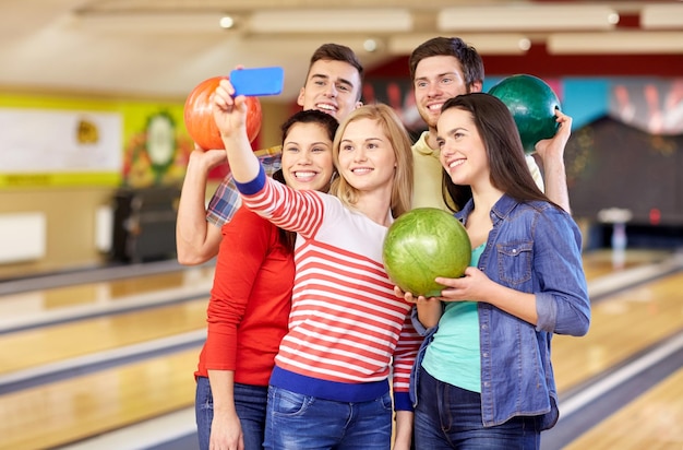 gente, ocio, deporte, amistad y concepto de entretenimiento - amigos felices tomando selfie con smartphone en el club de bolos