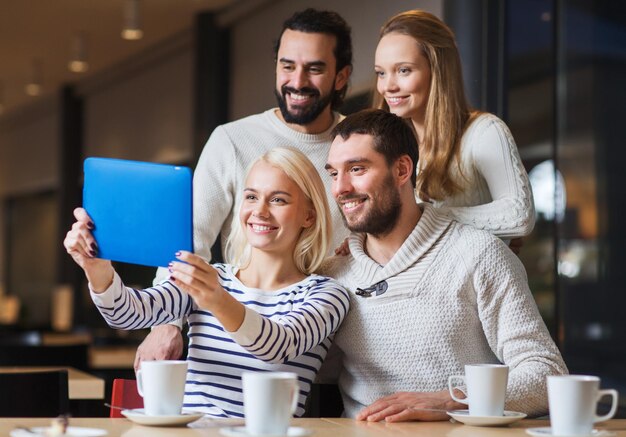 gente, ocio, tecnología y concepto de amistad - amigos felices con tablet pc tomando selfie en el café