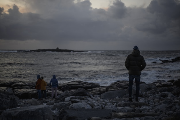 Gente en un oscuro paisaje marino con rocas y nubes