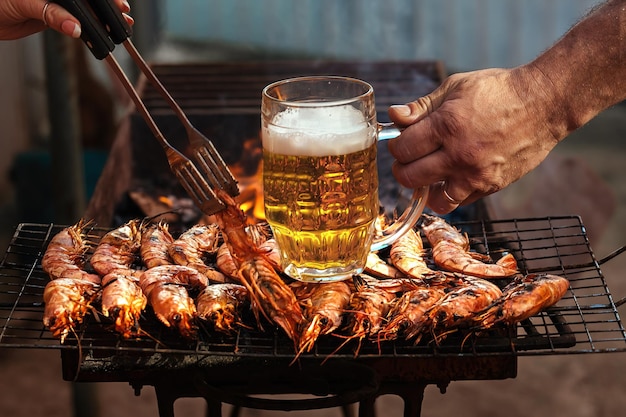 Gente de picnic cocina langostinos al fuego con cerveza fría