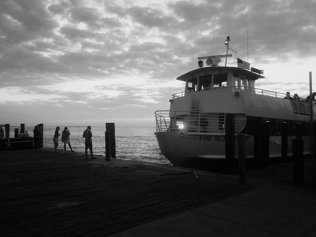 Foto gente de pie en el muelle por barco contra el cielo nublado