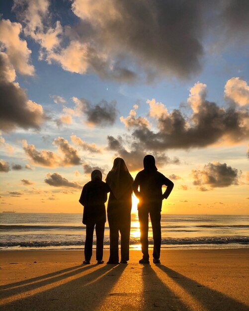 Gente de pie en la playa contra el cielo durante la puesta de sol