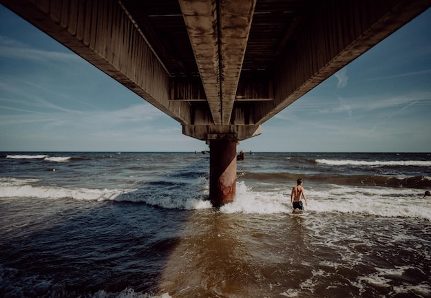 Foto la gente en la playa por el puente contra el cielo