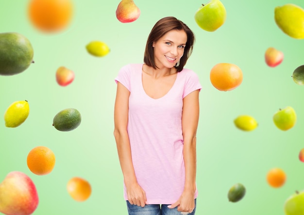 gente, publicidad, dieta, comida y concepto de alimentación saludable - mujer feliz con camiseta rosa en blanco sobre frutas de fondo verde