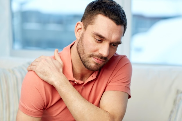 gente, salud y concepto de problema - hombre infeliz que sufre de dolor de cuello o hombro en casa