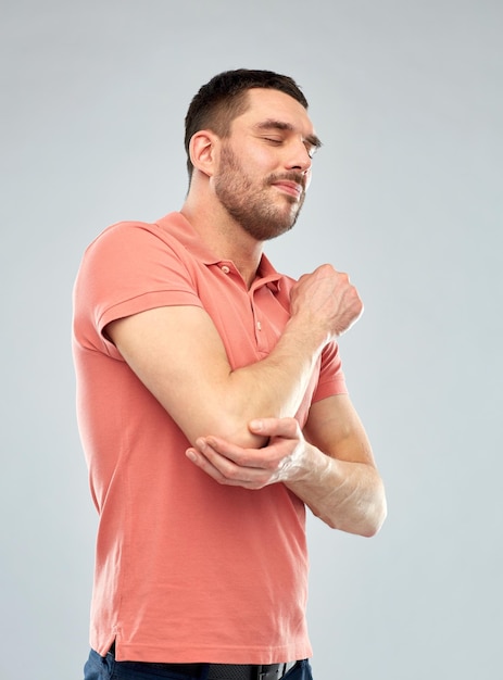 Foto gente, salud y concepto de problema - hombre infeliz que sufre de dolor en la mano sobre fondo gris