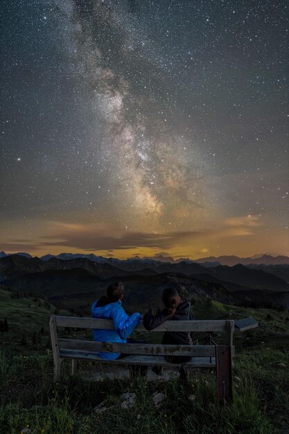 Foto gente sentada en un banco en el campo contra el cielo por la noche