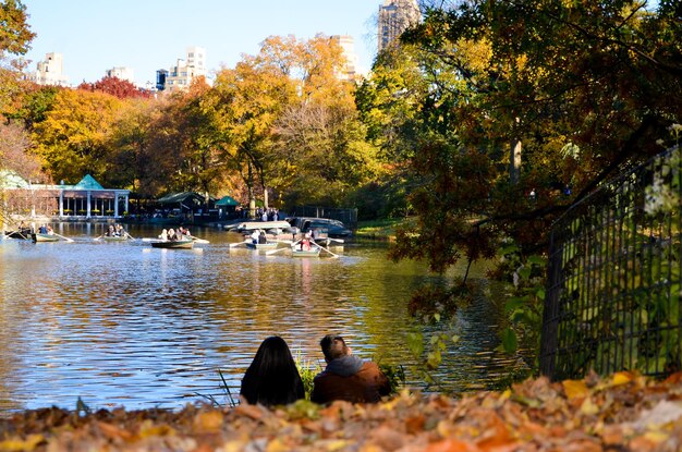 Foto gente sentada junto al lago durante el otoño en el central park en la ciudad de nueva york