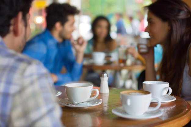 Foto gente sentada en una mesa con tazas de café y un hombre con una camisa azul en el fondo