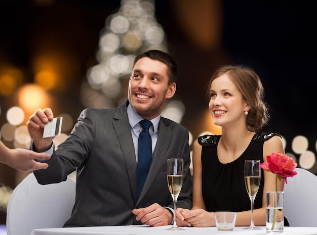 gente servicio y vacaciones concepto pareja sonriente pagando la cena con tarjeta de crédito en el restaurante sobre el fondo del árbol de Navidad