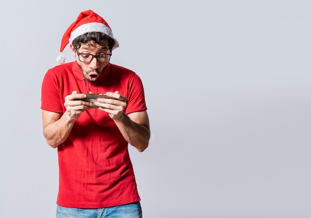 Gente sorprendida viendo una promoción navideña por teléfono Hombre asombrado mirando una oferta navideña en línea Chico mirando una promoción navideña por teléfono Concepto de ofertas especiales navideñas en línea