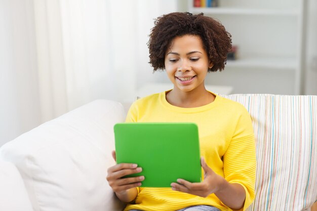 gente, tecnología y concepto de ocio - feliz mujer joven afroamericana sentada en un sofá con una computadora de tablet pc en casa