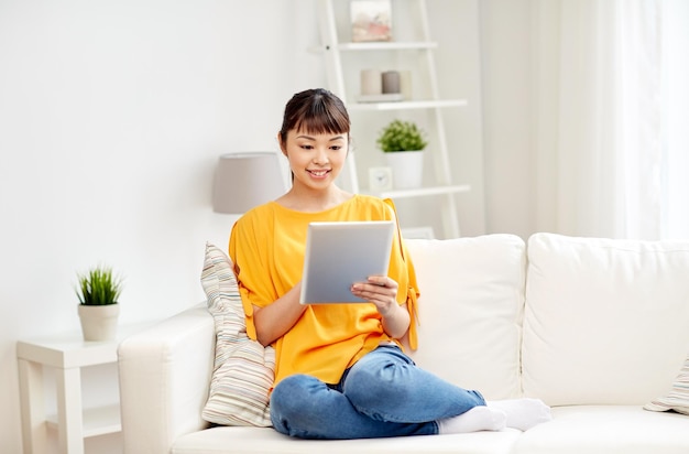 gente, tecnología y concepto de ocio - mujer asiática joven feliz sentada en un sofá con una computadora de tablet pc en casa