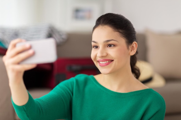 gente, tecnología y concepto de ocio - mujer asiática joven feliz tomando selfie en el teléfono inteligente en casa