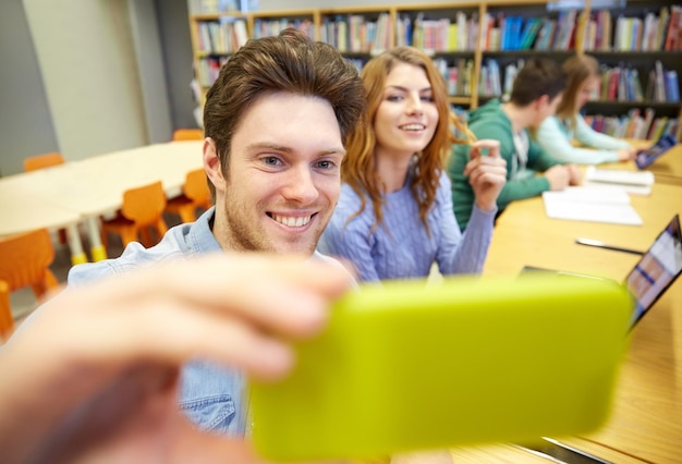 gente, tecnología, educación y concepto escolar - estudiantes felices o amigos con smartphone tomando selfie en la biblioteca