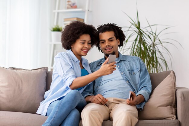 gente, tecnología, internet y concepto de comunicación - pareja feliz con smartphones en casa