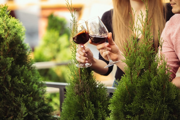 Gente tintineo de vasos con vino en la terraza de verano de cafetería o restaurante. Amigos alegres felices celebran el festival de verano u otoño. Primer plano de manos humanas, estilo de vida.