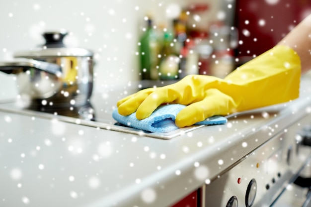 gente, trabajo doméstico y concepto de limpieza - cierre de la mano de la mujer en guante protector con cocina de limpieza de trapo en la cocina de casa sobre el efecto de la nieve