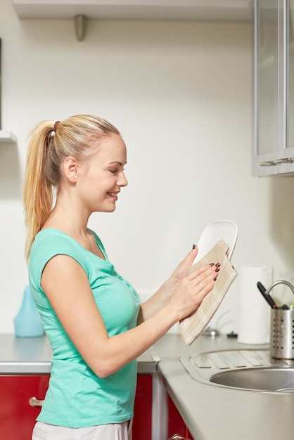 Foto gente, trabajo doméstico y concepto de limpieza - mujer feliz limpiando platos en la cocina de casa