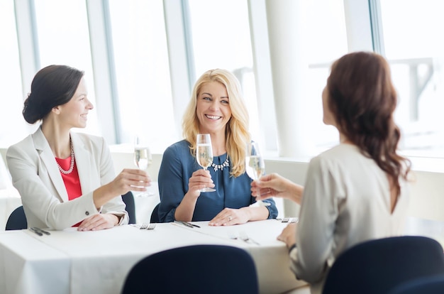 gente, vacaciones, celebración y concepto de estilo de vida - mujeres felices bebiendo champán en el restaurante