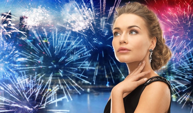 gente, vacaciones y concepto de glamour - hermosa mujer con aretes sobre fuegos artificiales en el fondo de la ciudad nocturna