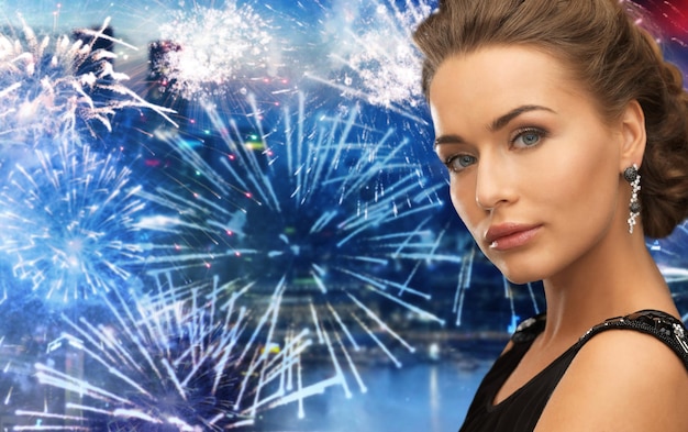 gente, vacaciones y concepto de glamour - hermosa mujer con aretes sobre fuegos artificiales en el fondo de la ciudad nocturna