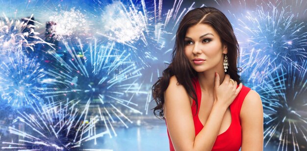 Foto gente, vacaciones y concepto de moda - hermosa mujer sexy vestida de rojo sobre fuegos artificiales en el fondo de la ciudad nocturna