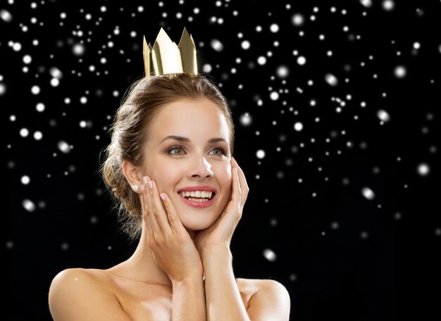 gente, vacaciones, concepto de realeza y glamour - mujer sonriente vestida de noche con corona dorada sobre fondo negro nevado