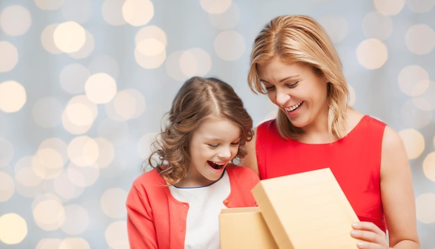 gente, vacaciones, navidad y concepto familiar - feliz madre e hija abriendo una caja de regalo sobre el fondo de las luces navideñas