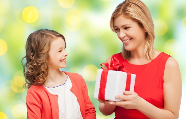 gente, vacaciones, navidad y concepto familiar - feliz madre e hija dando y recibiendo caja de regalo sobre fondo de luces verdes