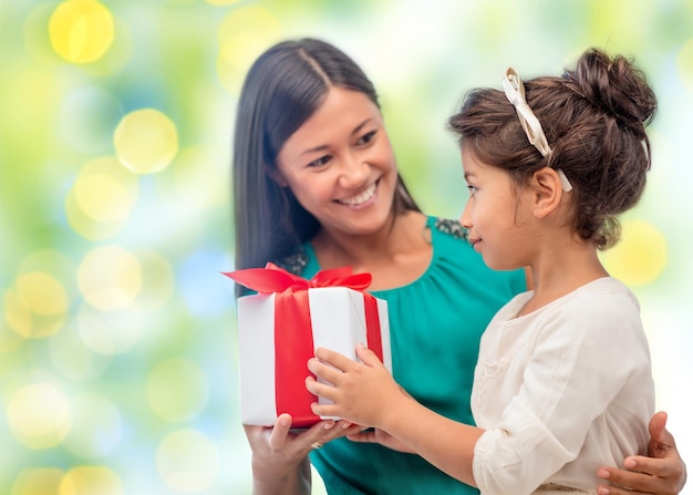 gente, vacaciones, navidad y concepto familiar - feliz madre e hija dando y recibiendo cajas de regalo sobre fondo de luces verdes navideñas