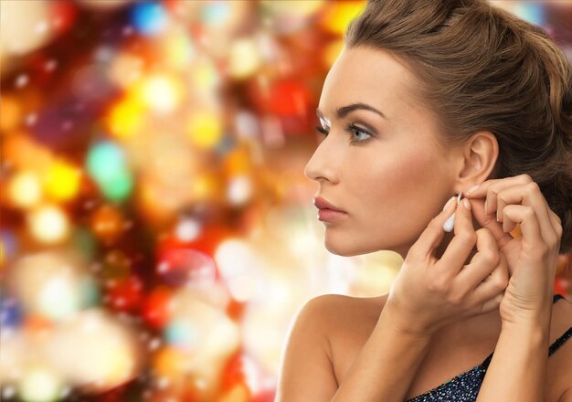 gente, vacaciones, navidad y concepto de glamour - cerca de una mujer hermosa que usa aretes sobre fondo de luces rojas