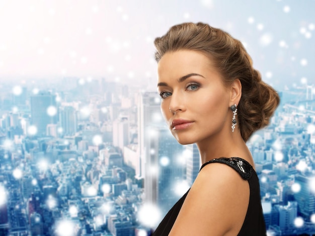gente, vacaciones, navidad y concepto de glamour - hermosa mujer vestida de noche con aretes sobre fondo nevado