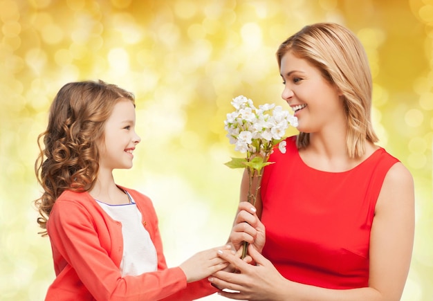 gente, vacaciones, relaciones y concepto familiar - pequeña hija feliz dando flores a su madre sobre fondo de luces amarillas