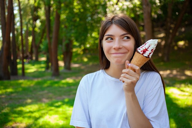 Gente de verano y concepto de comida chatarra Niña en auriculares inalámbricos con delicioso helado con cobertura de bayas en cono de galleta Espacio de copia vacío