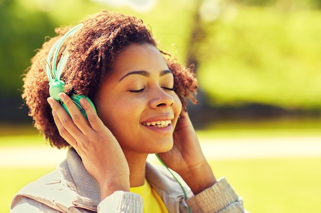 gente, verano, tecnología y concepto de ocio - cara feliz de una joven afroamericana con auriculares escuchando música al aire libre