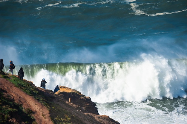 Gente viendo grandes olas en Nazaré, Portugal. En este lugar las olas más grandes del mundo debido al cañón submarino