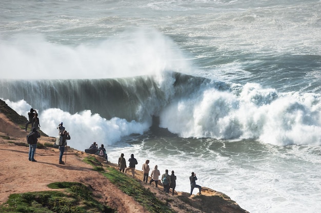 Gente viendo grandes olas en Nazaré, Portugal. Olas cruzando cerca de la orilla debido al cañón submarino