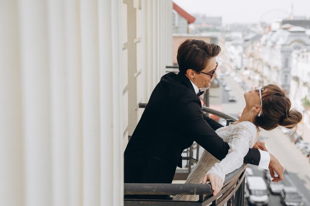 gentil y hermosa novia y el novio tomándose de la mano mirándose cerca del antiguo balcón de la cerca