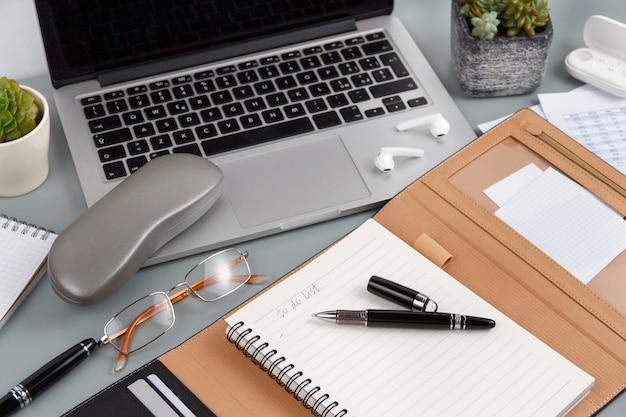 Geöffnete Agenda mit handgeschriebener TO DO LIST in der Nähe von Brille und Laptop auf einer grauen Nahaufnahme