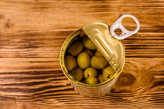 Geöffnete Blechdose mit grünen Oliven auf rustikalem Holztisch