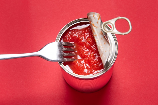 Geöffnete Blechdose mit Tomatenkonserven auf rotem Grund