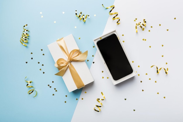 Geöffnete Geschenkbox mit goldenem Band und Smartphone auf farbigem Hintergrund Draufsicht Leere offene Box Verpackungsmodell Vorlage für Ihr Design-Branding-Modell